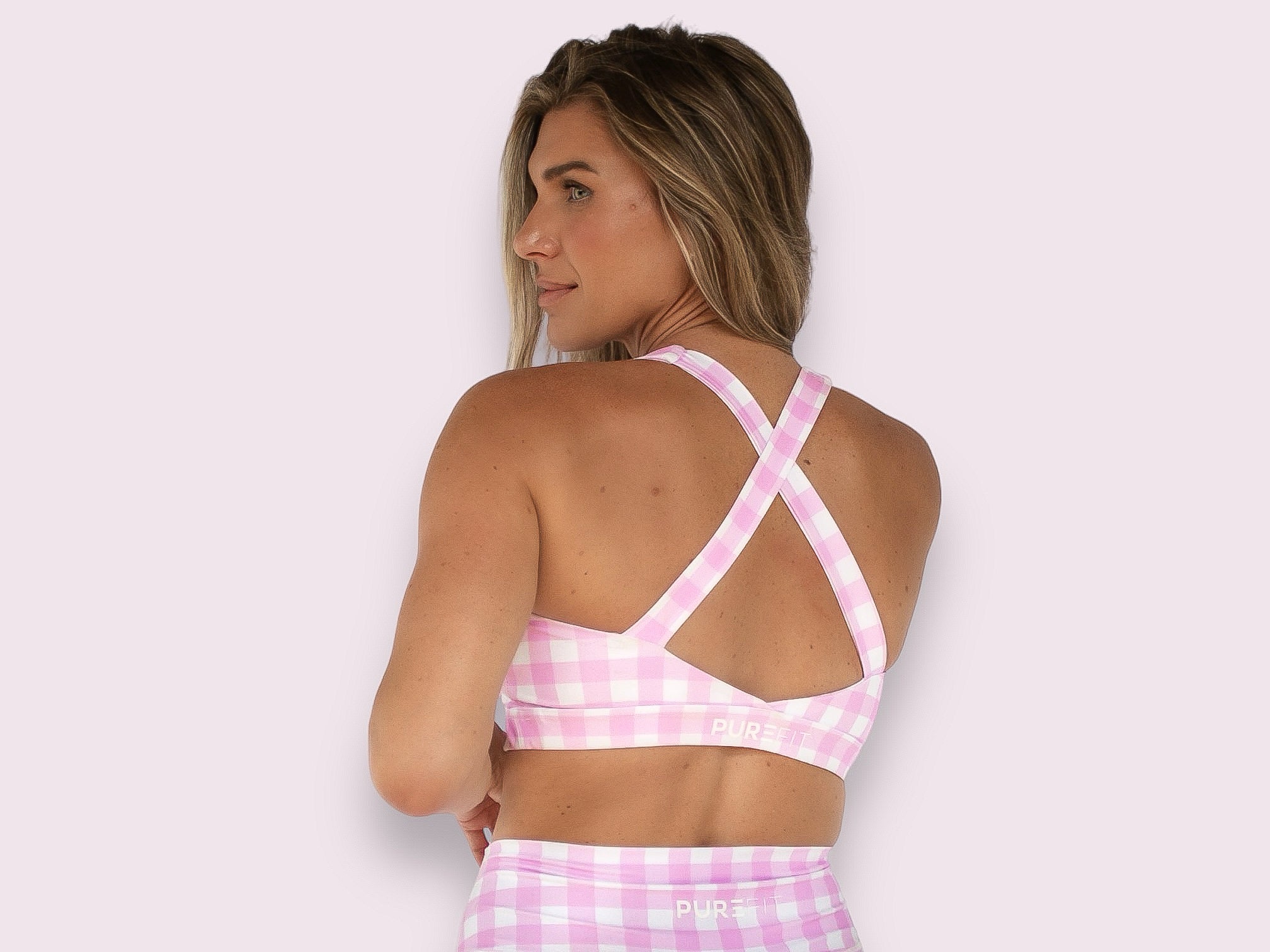Woman wearing a pink and white checkered sports bra with a light pink background.
