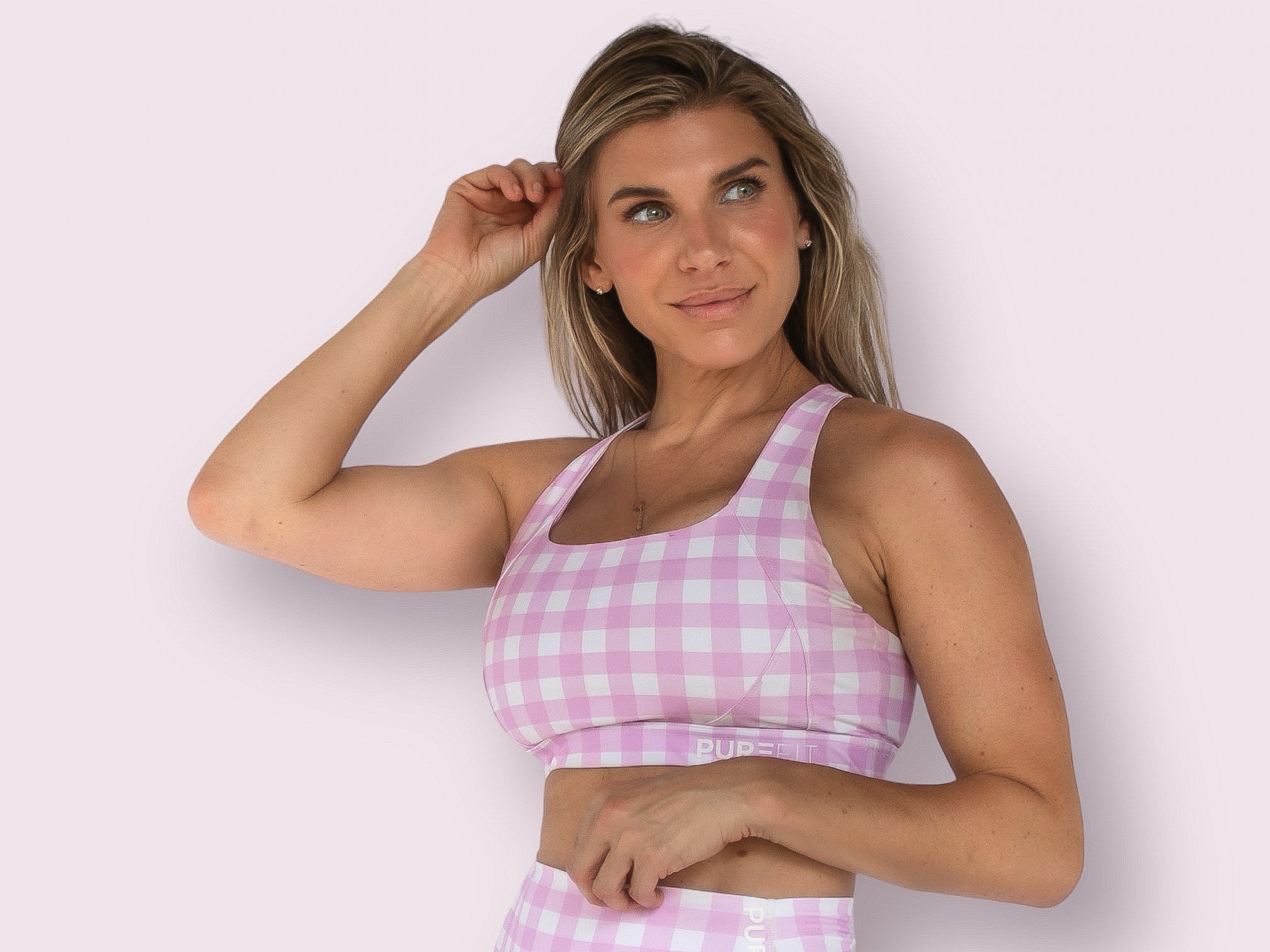 Woman wearing a pink and white checkered sports bra with a light pink background