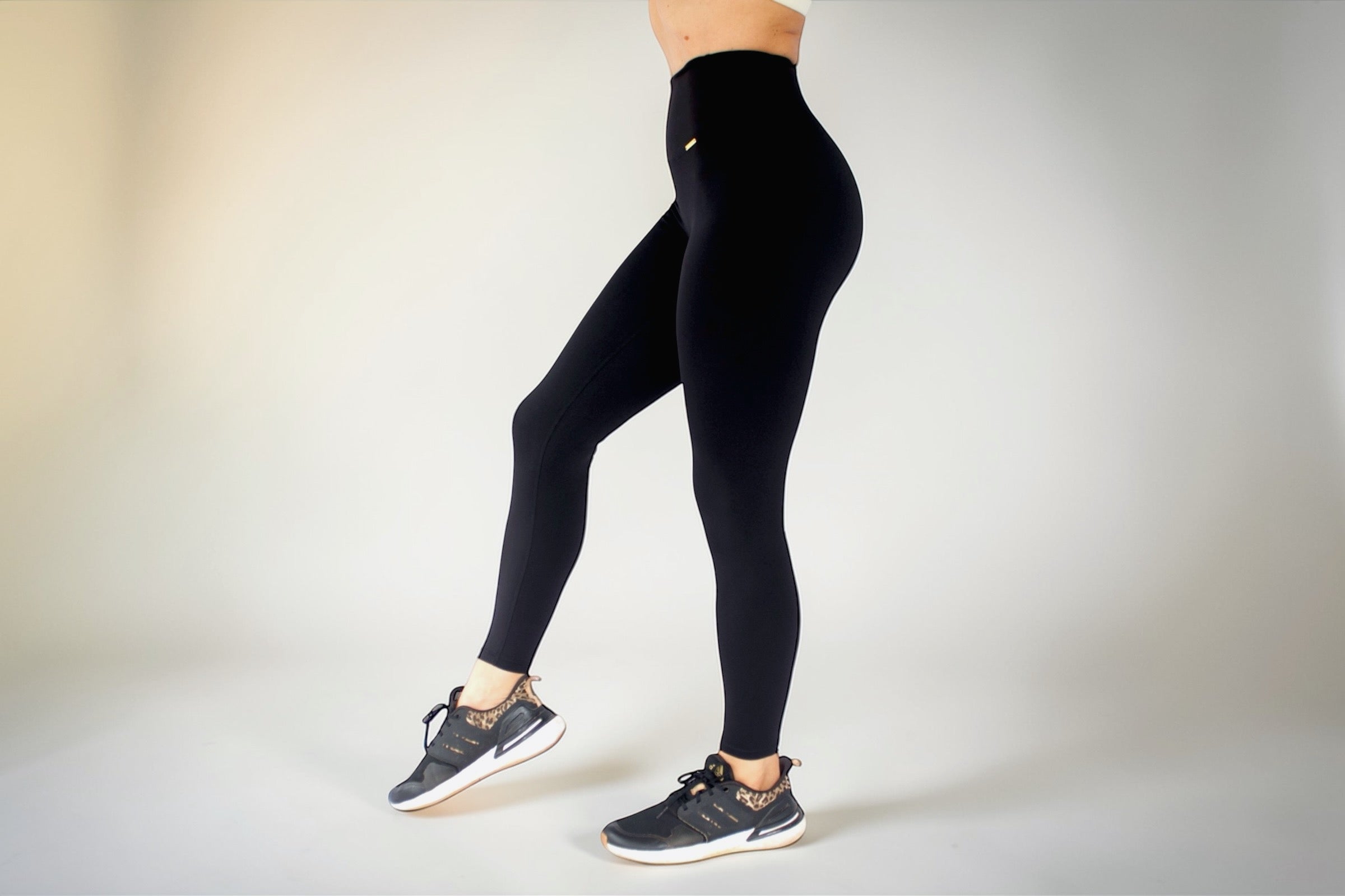 Person wearing black leggings and sneakers on a plain background