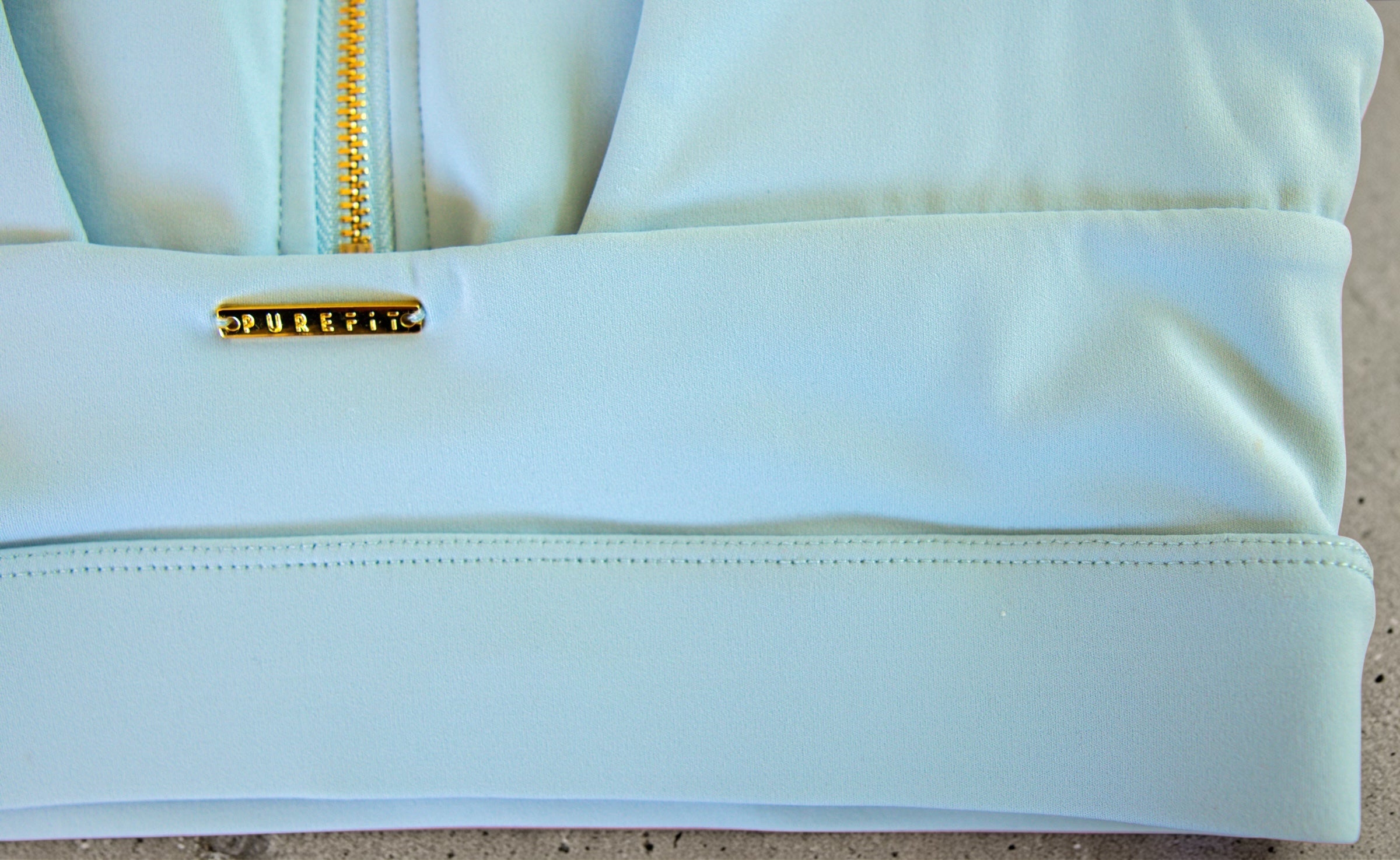 Detail picture of the back of the light blue gold zipper sports bra with brand logo on a neutral background