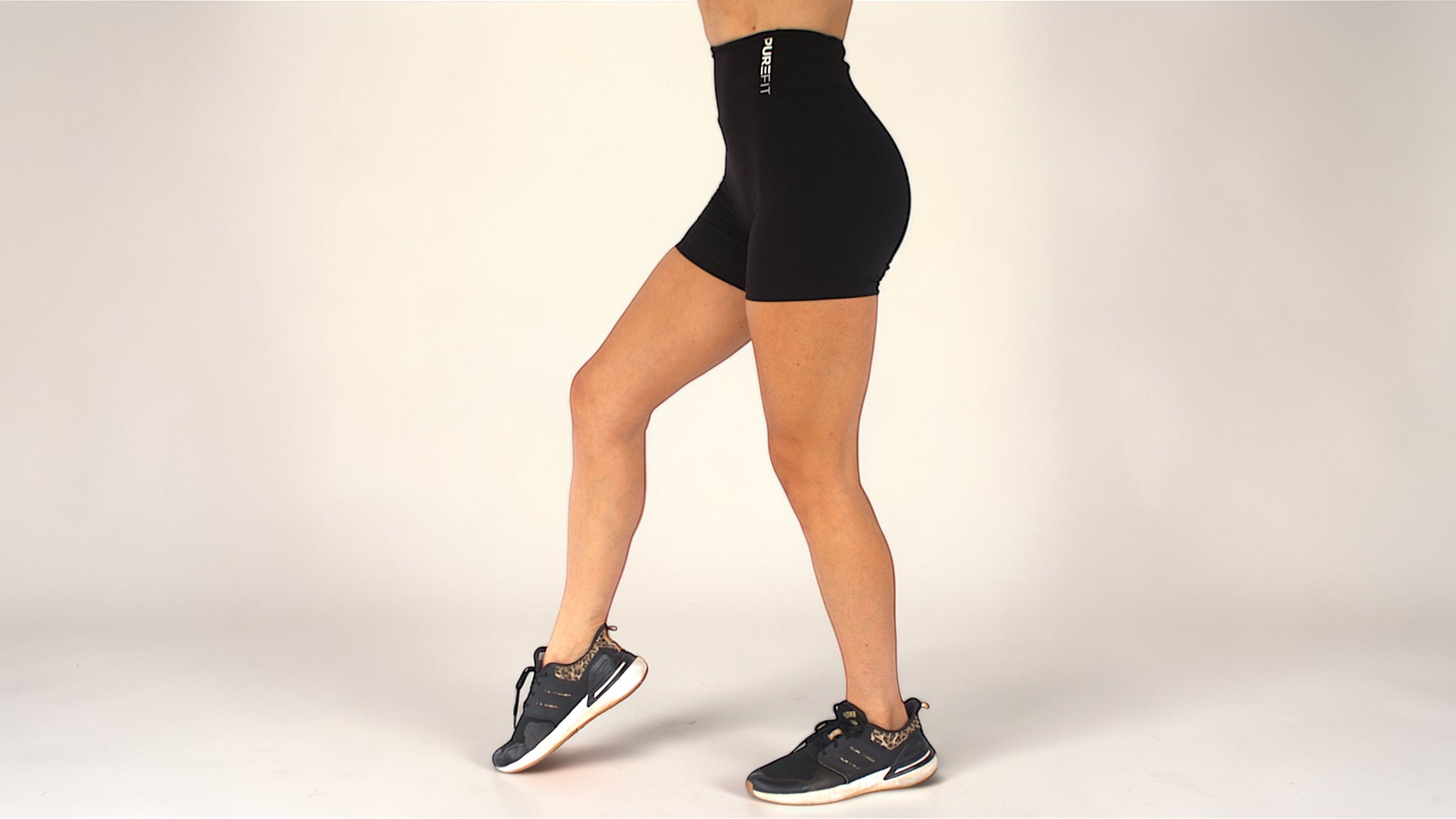 Person wearing black athletic shorts and shoes on a plain background