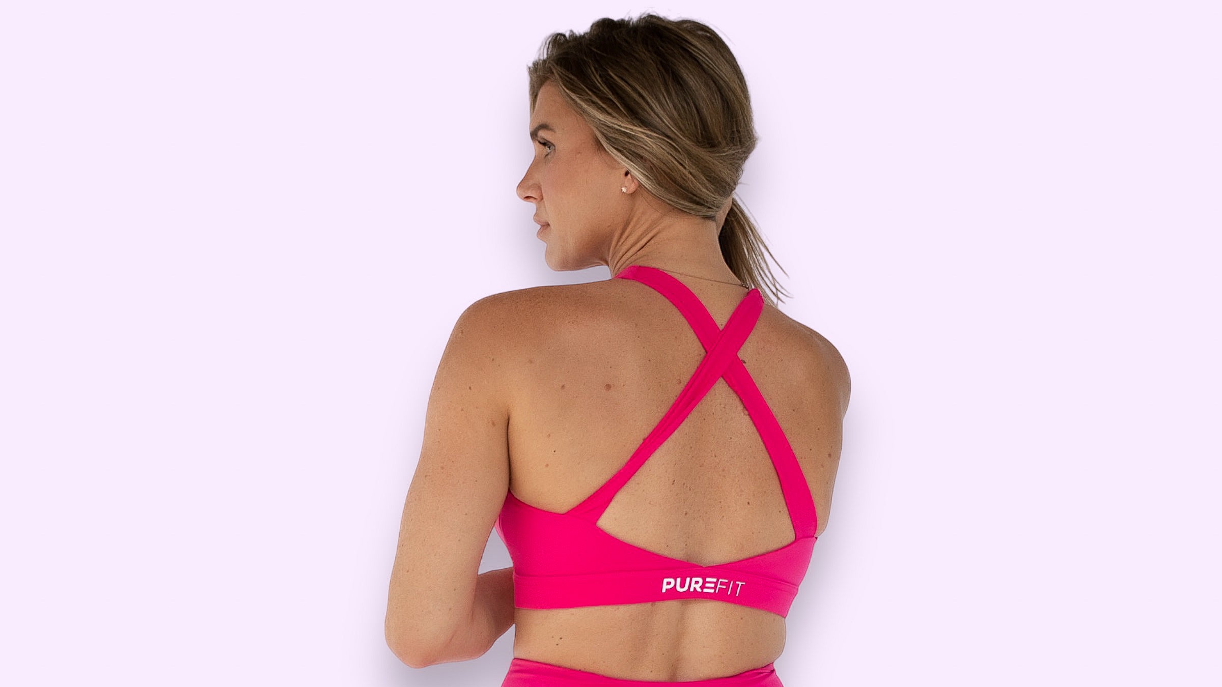 Woman showing the back of a hot pink sports bra standing in front of a neutral background.