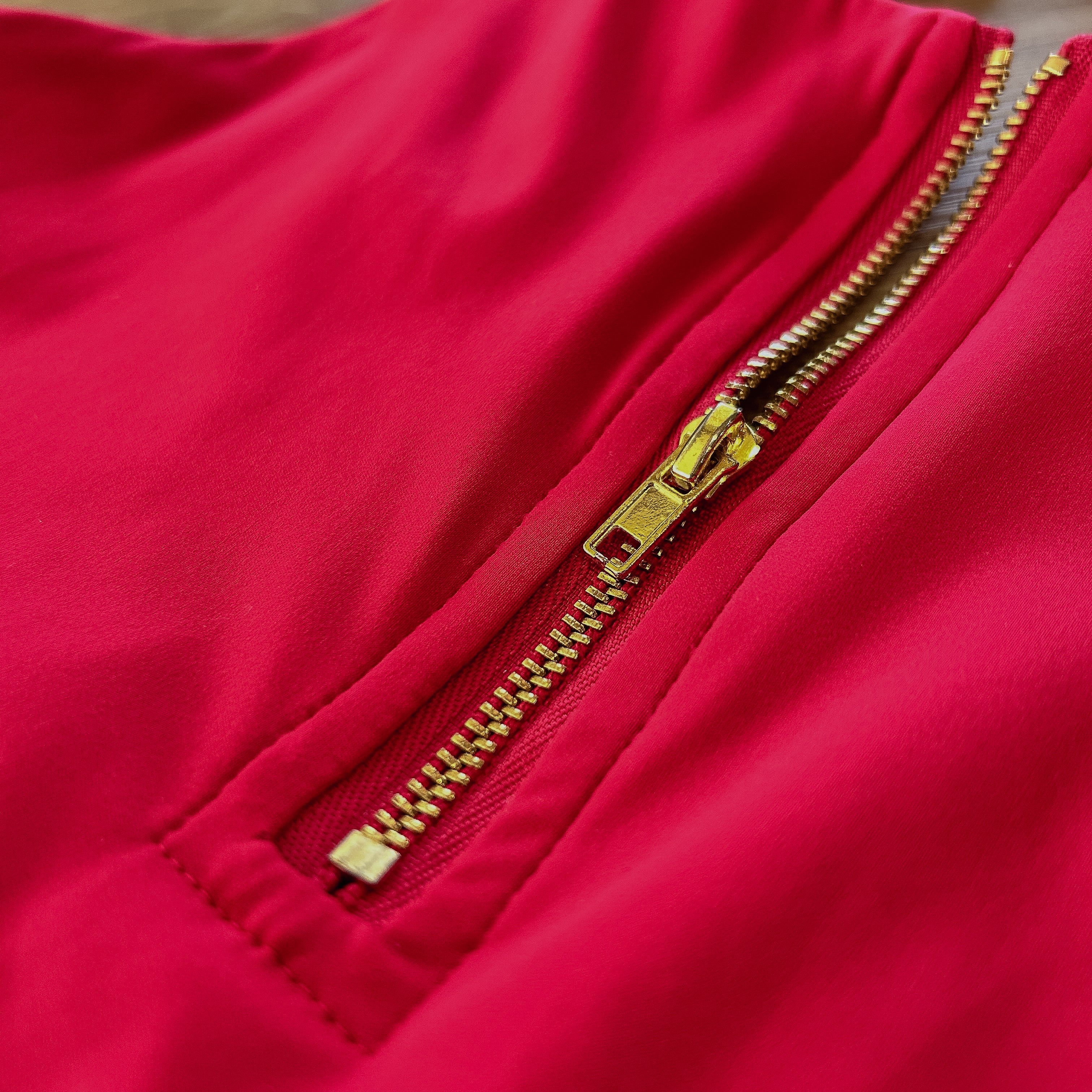 up close detailed picture of the red sports bra that features a gold zipper.
