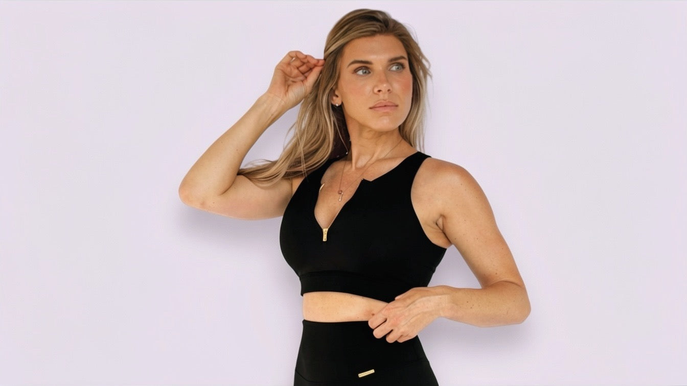 Woman wearing a black sports bra with a zip feature on the front,  standing against a white background